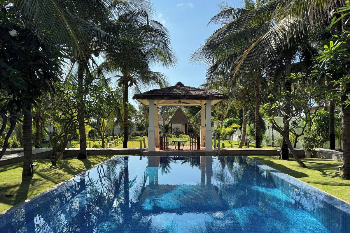 A clear blue pool surrounded by palm trees and a gazebo.