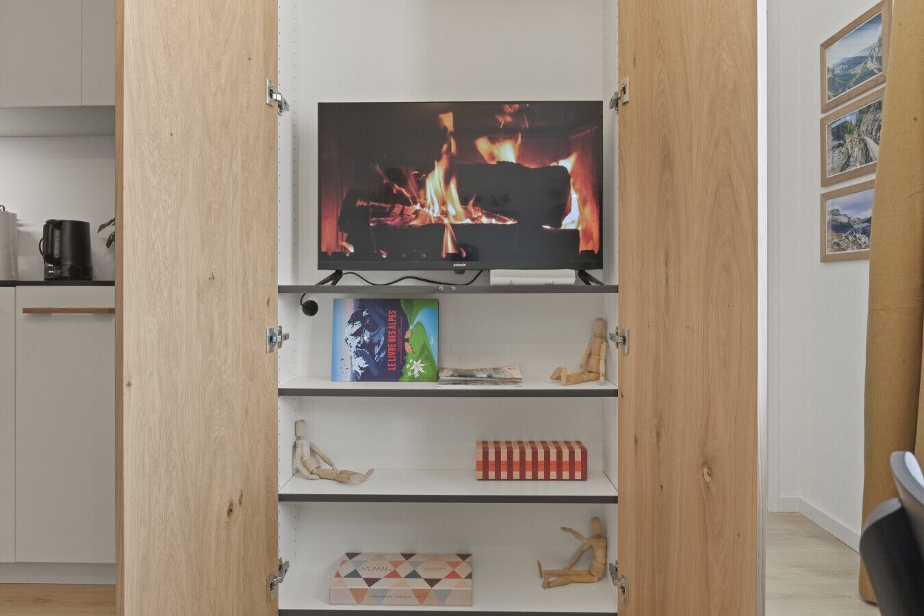 A room with a television on a shelf, a wooden cabinet, and a shelf with books and a small wooden figure.