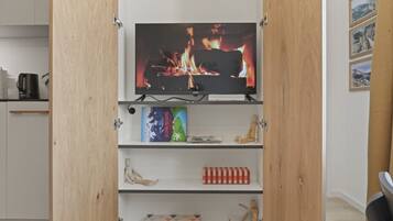 A room with a television on a shelf, a wooden cabinet, and a shelf with books and a small wooden figure.