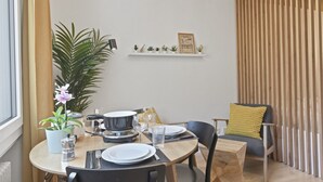 A dining area with a round table set for two, a potted plant, and a shelf with decorative items. - Élégant studio, proche des bains & nature (Leukerbad)