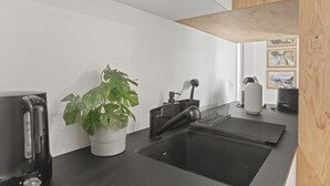 A modern kitchen with a black countertop, a sink, a coffee maker, and a potted plant. - Élégant studio, proche des bains & nature (Leukerbad)