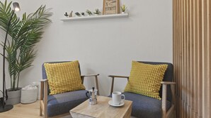 A cozy seating area with two chairs, a small table, and a shelf with plants and a framed picture. - Élégant studio, proche des bains & nature (Leukerbad)