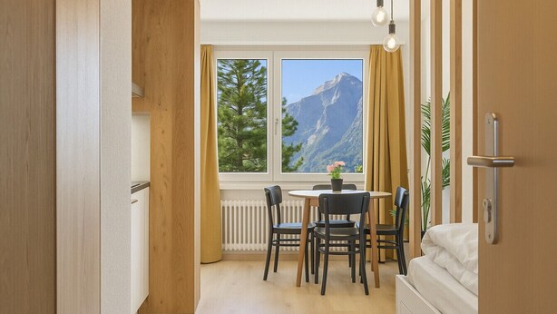 A modern kitchen with a dining area, large windows with a mountain view, and a small table with chairs. - Élégant studio, proche des bains & nature (Leukerbad)