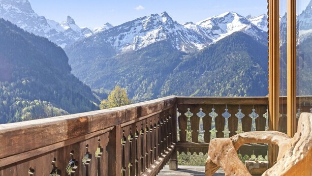 A wooden balcony with a view of snow-capped mountains and a forested valley.