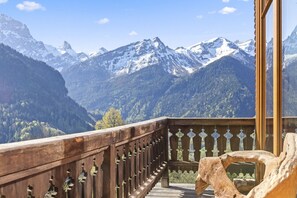 A wooden balcony with a view of snow-capped mountains and a forested valley.