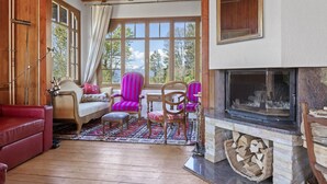 A cozy room with a fireplace, wooden furniture, and large windows offering a view of the outdoors.