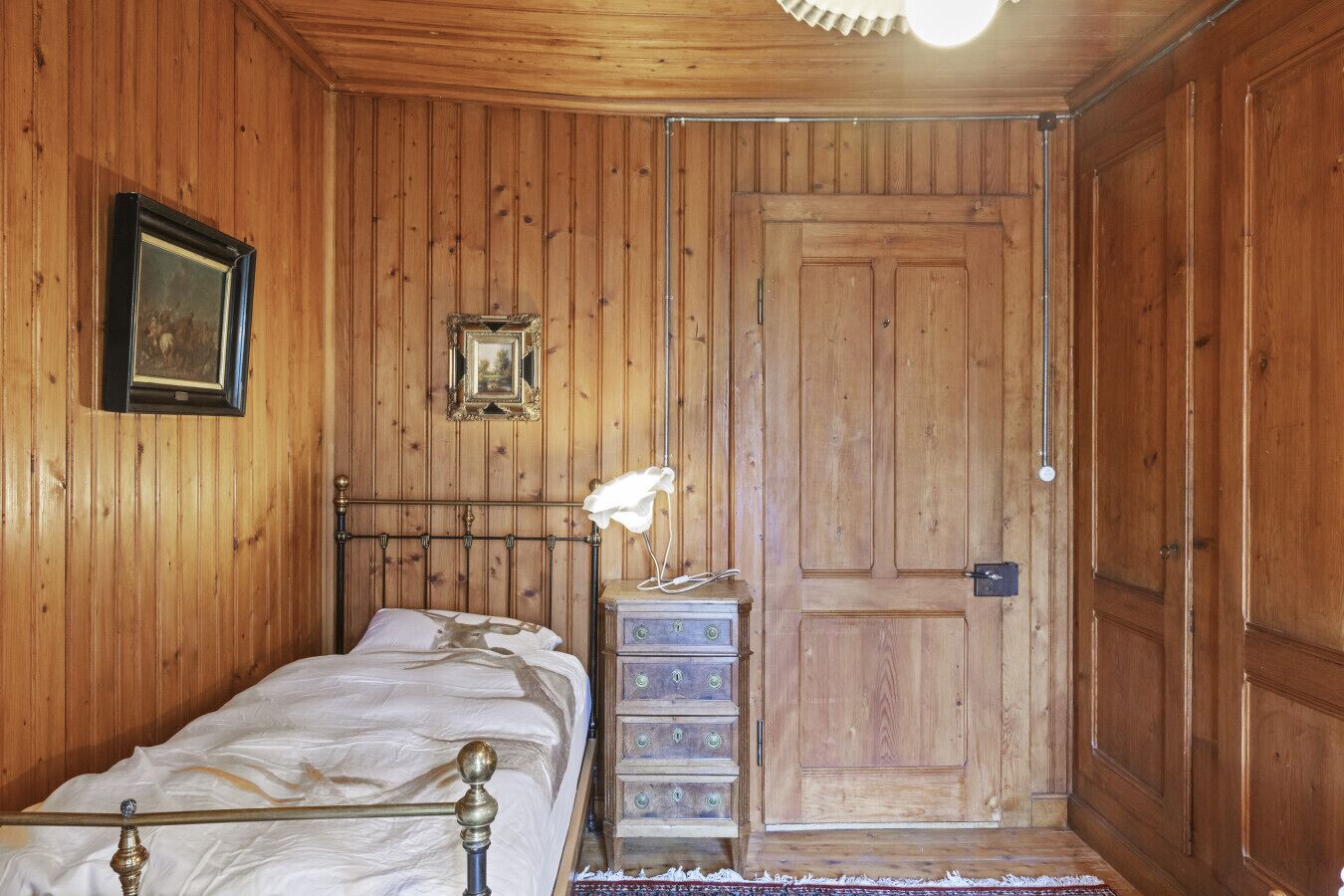 Ein Zimmer mit Holzwänden, einem Bett, einer Kommode und einer Tür.