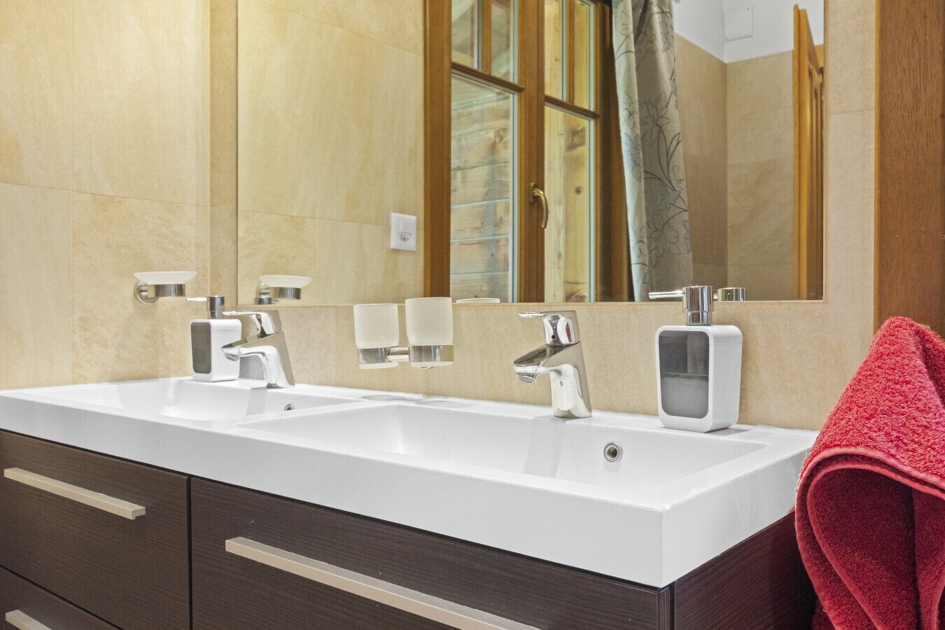 Un baño moderno con lavamanos doble, dos grifos, un espejo y una toalla roja.