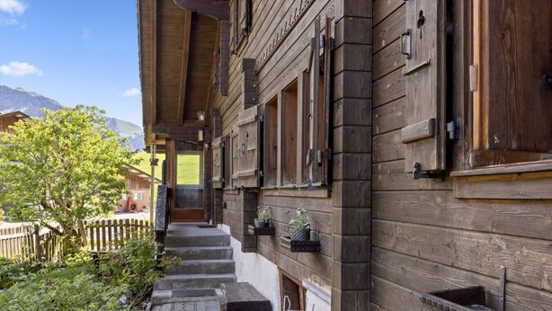 Il s’agit d’un bâtiment en bois, doté d’un escalier en bois menant à une porte. On y trouve des fenêtres et un petit jardin avec des plantes.