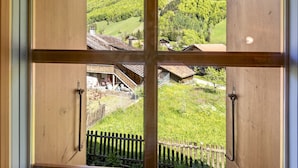 Une fenêtre à cadre en bois donnant sur un paysage rural, avec des maisons et une clôture en bois.