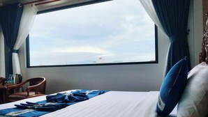 A hotel room with a bed, a chair, a table with a kettle, and a view of the sky through a large window. - Cozy 86 Homestay (Can Tho)
