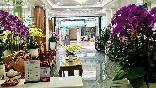 A hotel lobby with ornate wood furniture, a chandelier, and potted orchids. - Cozy 86 Homestay (Can Tho)