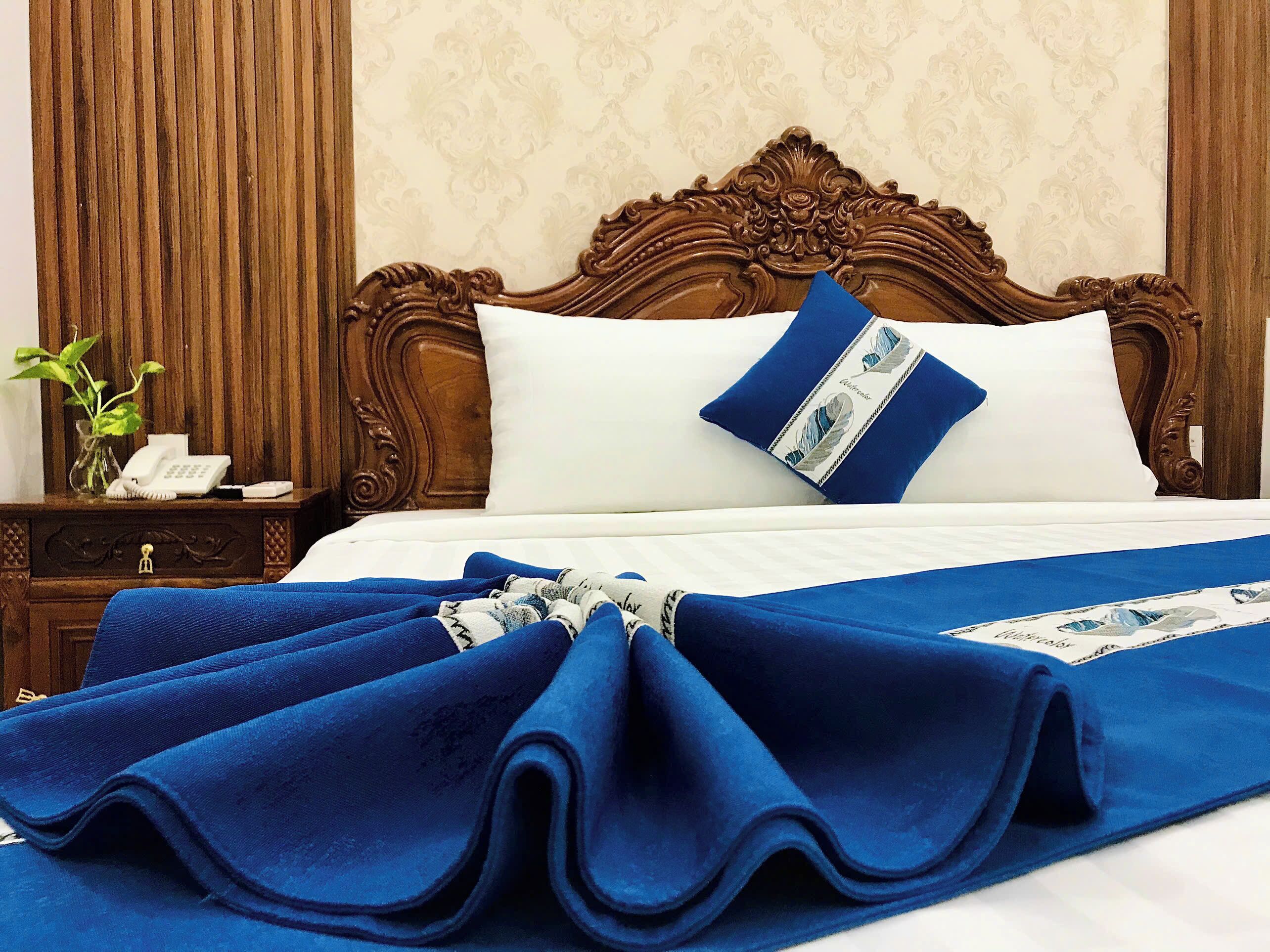 A neatly made bed with a blue blanket, a white pillow, and a decorative pillow with a blue and white pattern.
