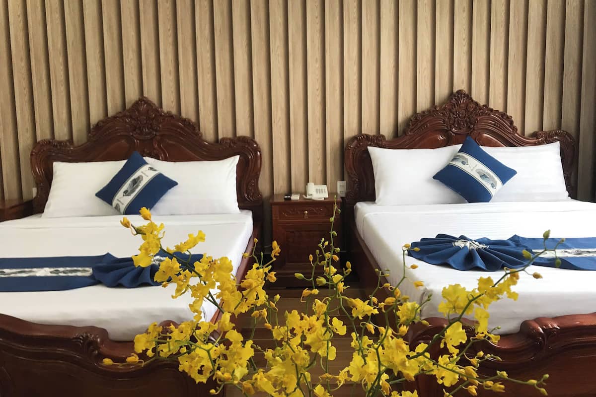 Two wooden beds with white linens and blue accents, a wooden nightstand with a phone, and a wall with vertical wooden slats.