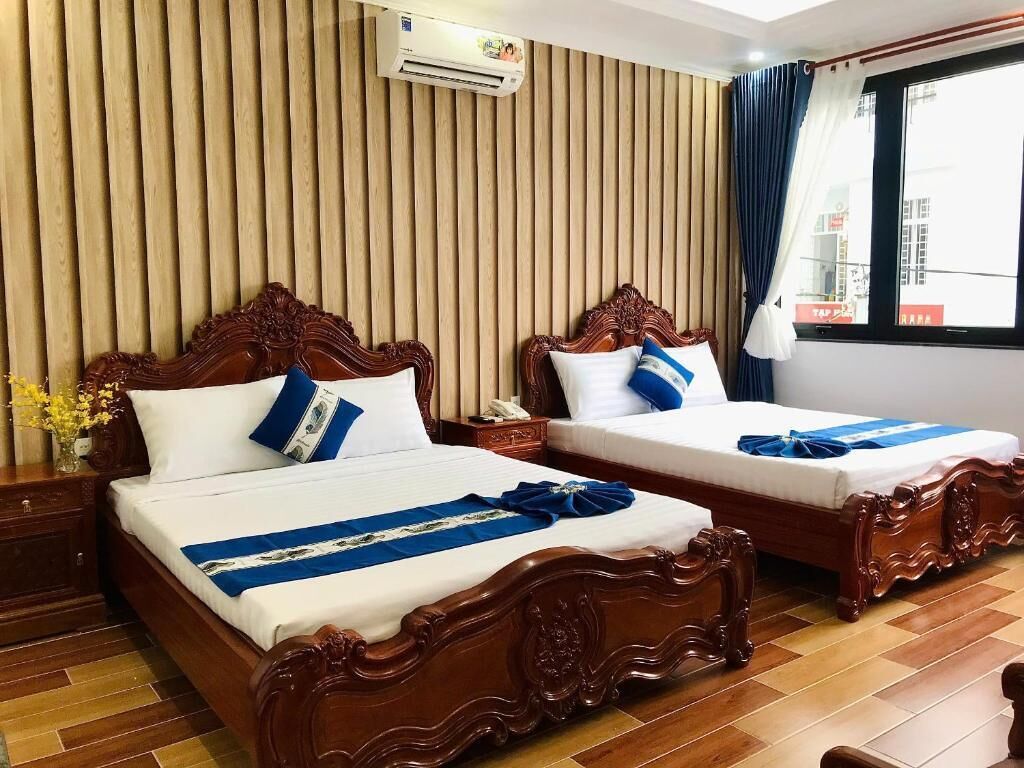 A hotel room with two wooden beds, a wooden floor, a vertical wooden panel wall, and a window with curtains.