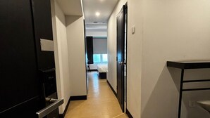 Un estrecho pasillo con piso de madera que conduce a un dormitorio con ventana.