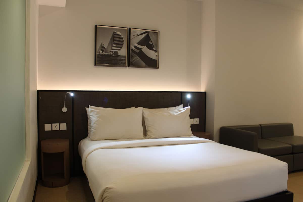 A neatly made bed with white linens, a dark headboard, and two framed pictures on the wall.