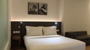 Una cama bien hecha con sábanas blancas, un cabecero oscuro y dos cuadros en la pared.