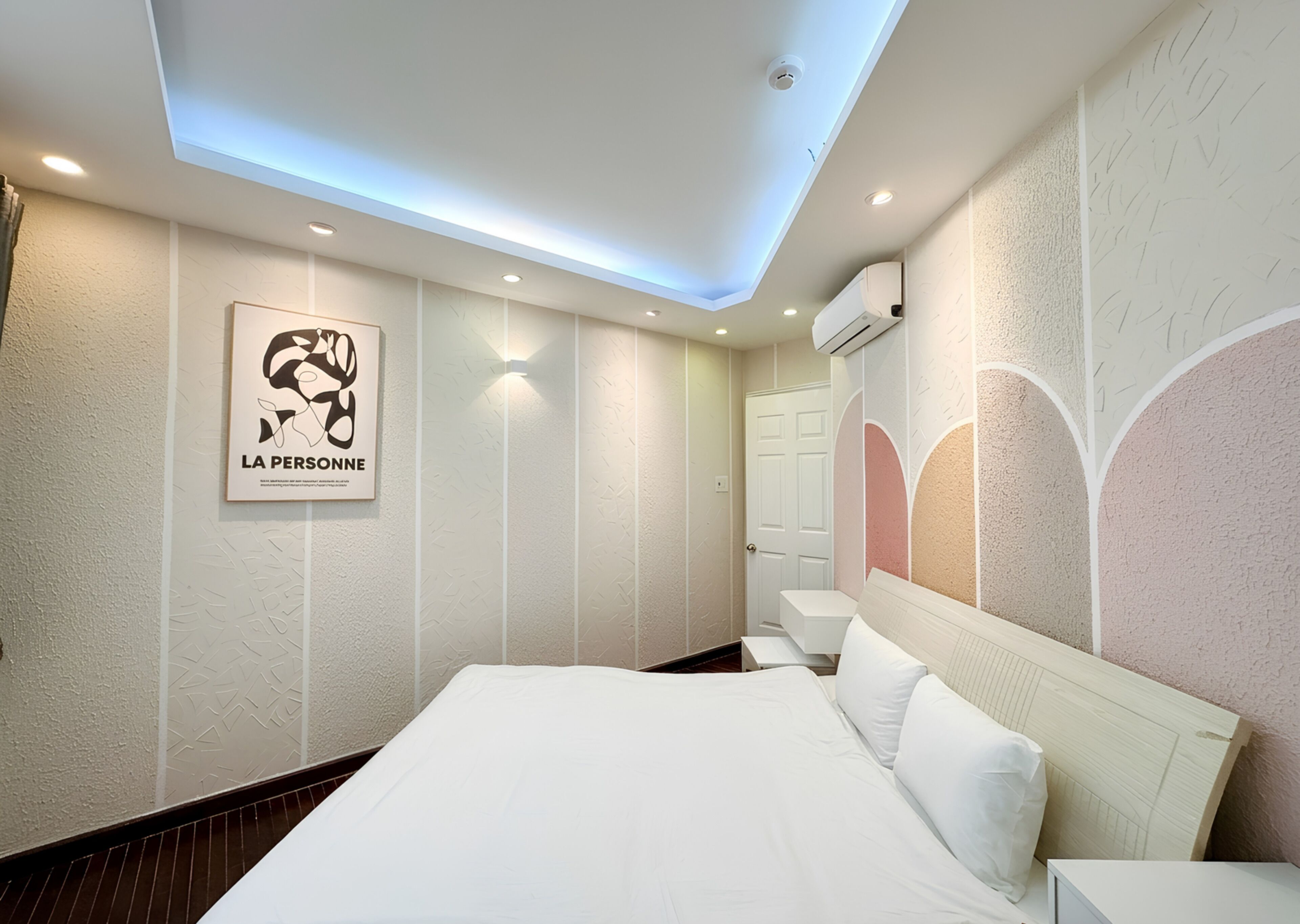 Ein Hotelzimmer mit einem Bett, einem Wandbild, deckenmontierter Beleuchtung und einer Klimaanlage.