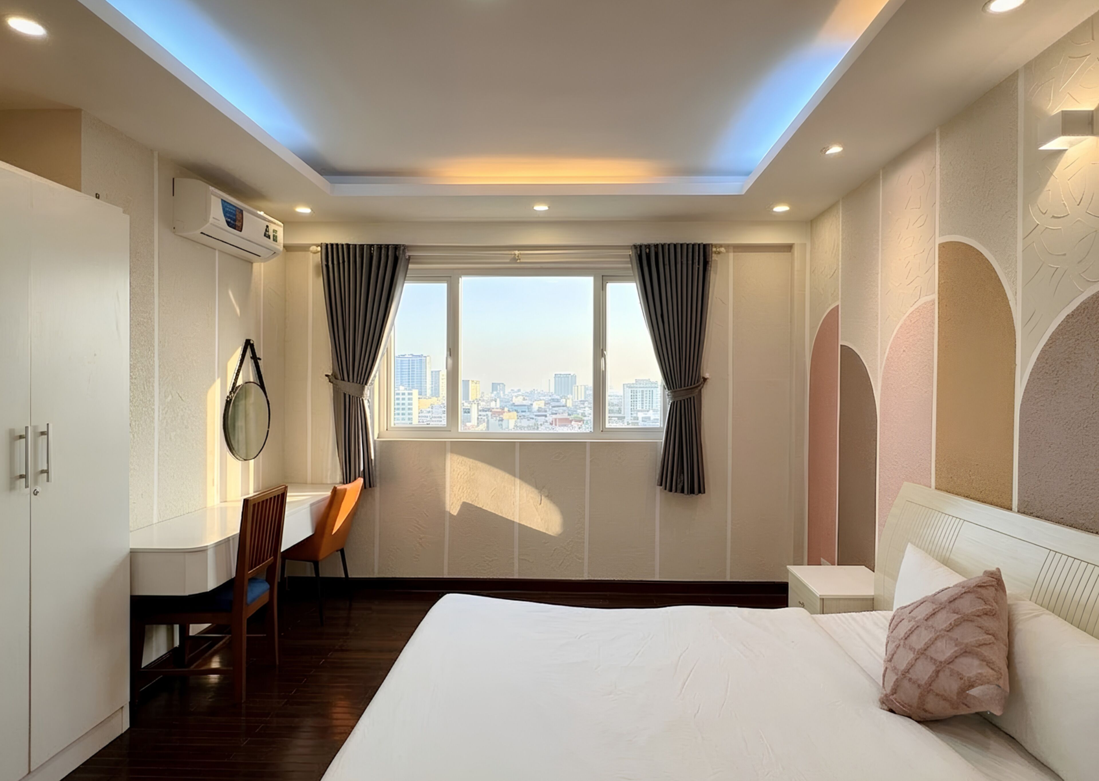 Quarto de hotel com cama, escrivaninha, cadeira, janela com cortinas, ar condicionado e vista para a paisagem urbana.