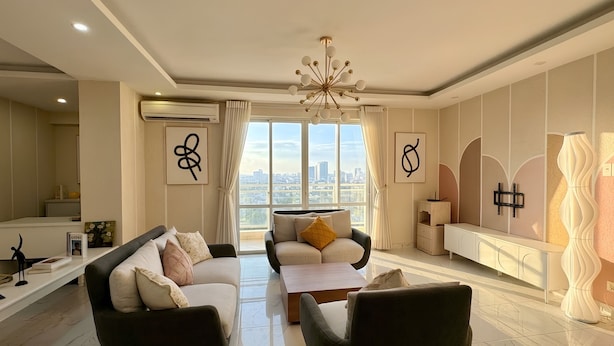 Un salon moderne avec un canapé, des fauteuils, une table basse et une vue sur la ville grâce à de grandes fenêtres.