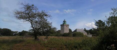 Un faro con base de piedra y cúpula verde, rodeado por un campo cubierto de hierba y árboles.