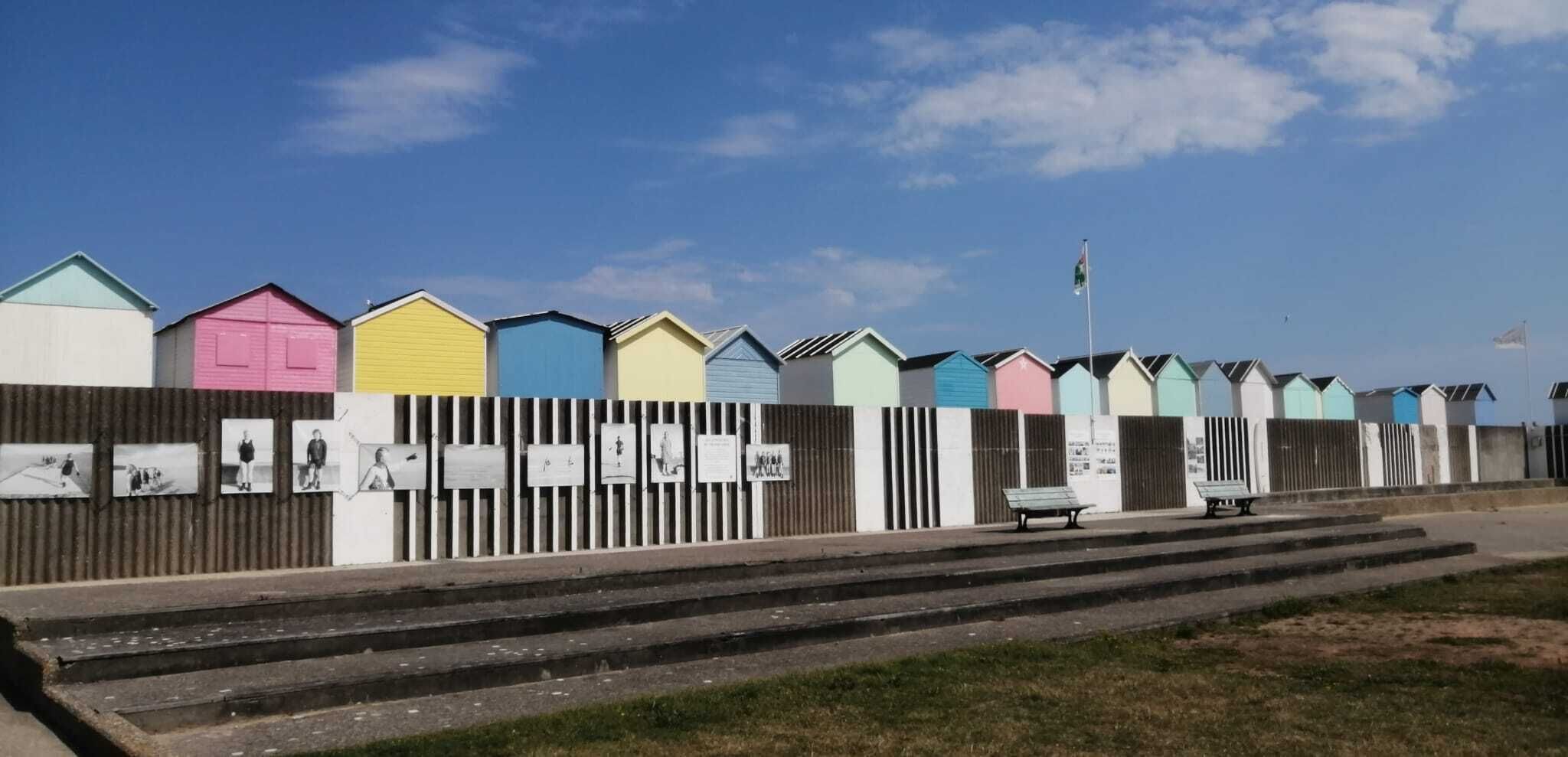 En rad färgglada strandhytter med ett korrugerat metallstaket i förgrunden.