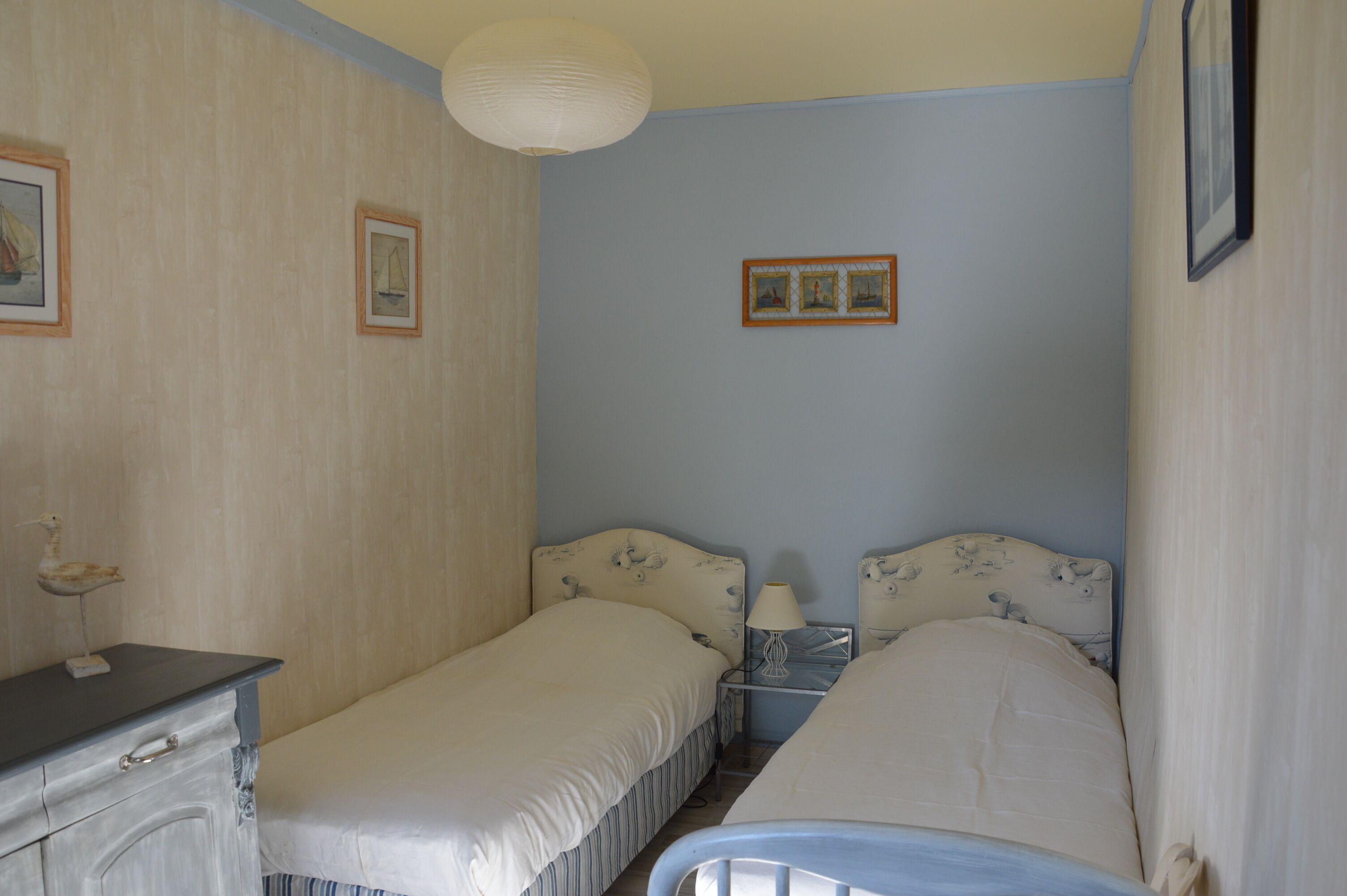 Ein Schlafzimmer mit zwei Einzelbetten, einem Schminktisch, einem Nachttisch mit Lampe sowie gerahmten Bildern an der Wand.