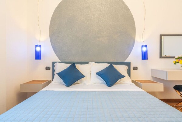A hotel room with a large bed, two nightstands, a bedside table, a wall-mounted mirror, and a large abstract wall decoration.
