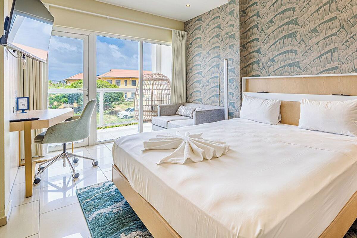 A hotel room with a large bed, a desk, a chair, and a view of the outside.