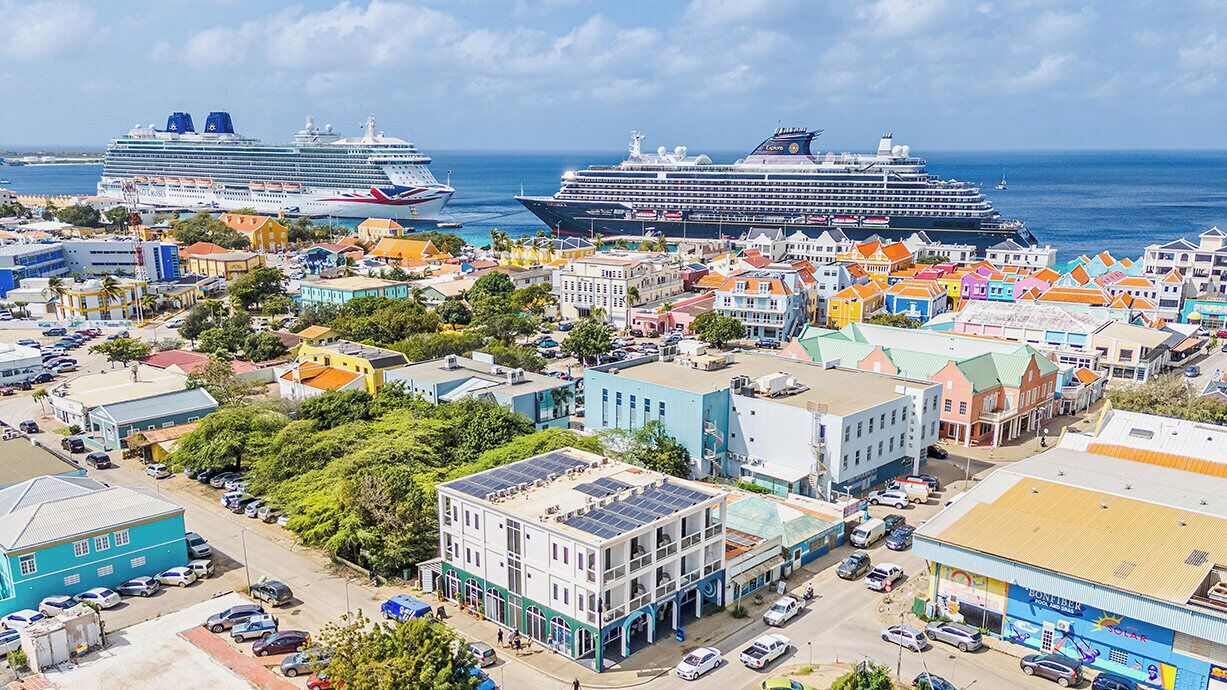 A coastal town with colorful buildings, a marina with cruise ships, and a prominent solar-powered building.