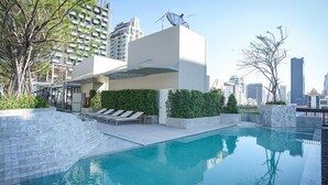 Una piscina sul tetto con lettini, un edificio moderno con tetto piatto e uno skyline sullo sfondo.