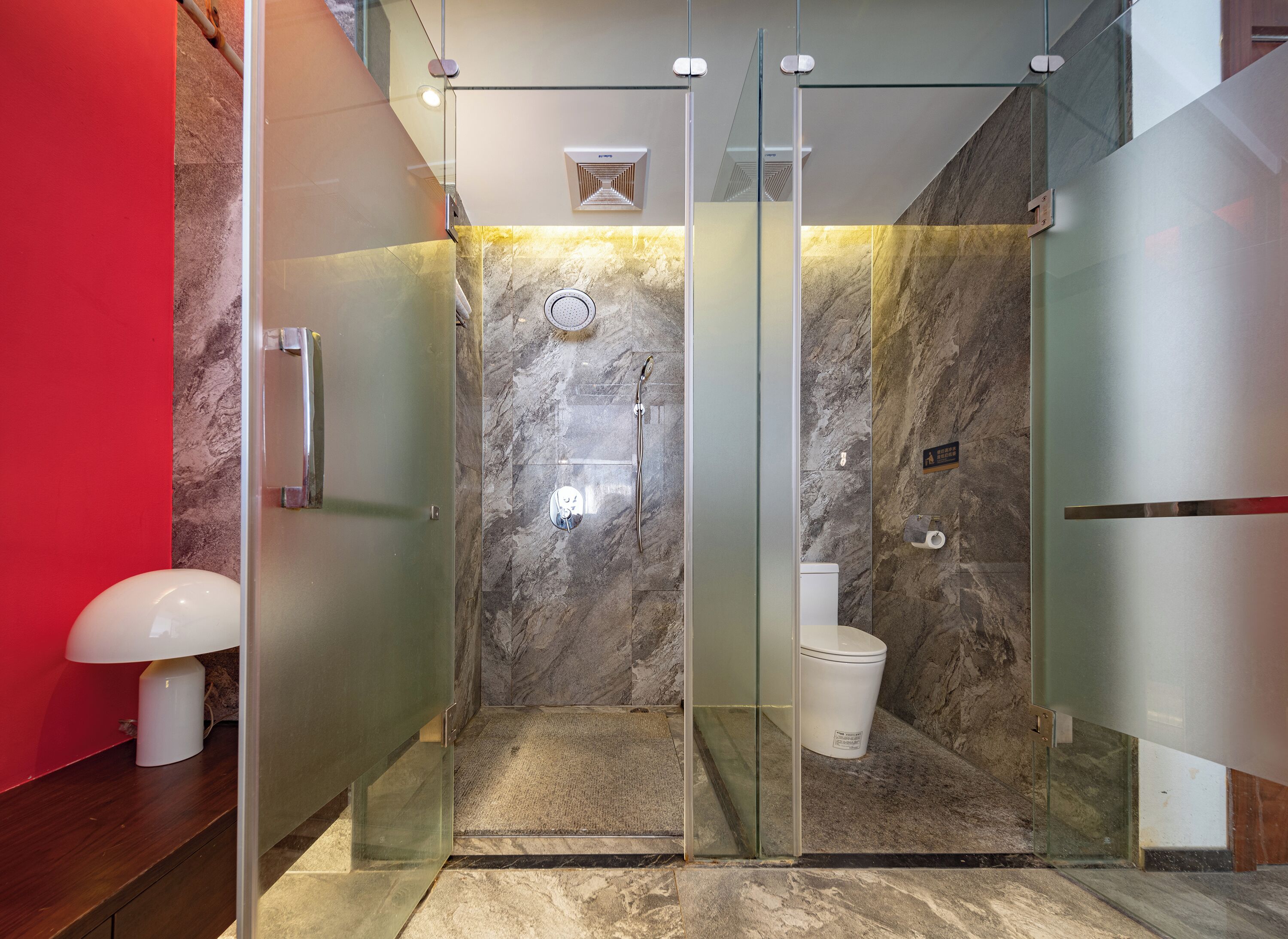 A modern bathroom with a glass-enclosed shower, marble walls, a toilet, and a hand dryer.