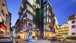 A multi-story hotel with a traditional architectural style, featuring a prominent entrance with a sign, multiple balconies, and a courtyard area with outdoor seating. - Riverside Peak Lodge Zhangjiajie Wulingyuan National Park (Zhangjiajie)