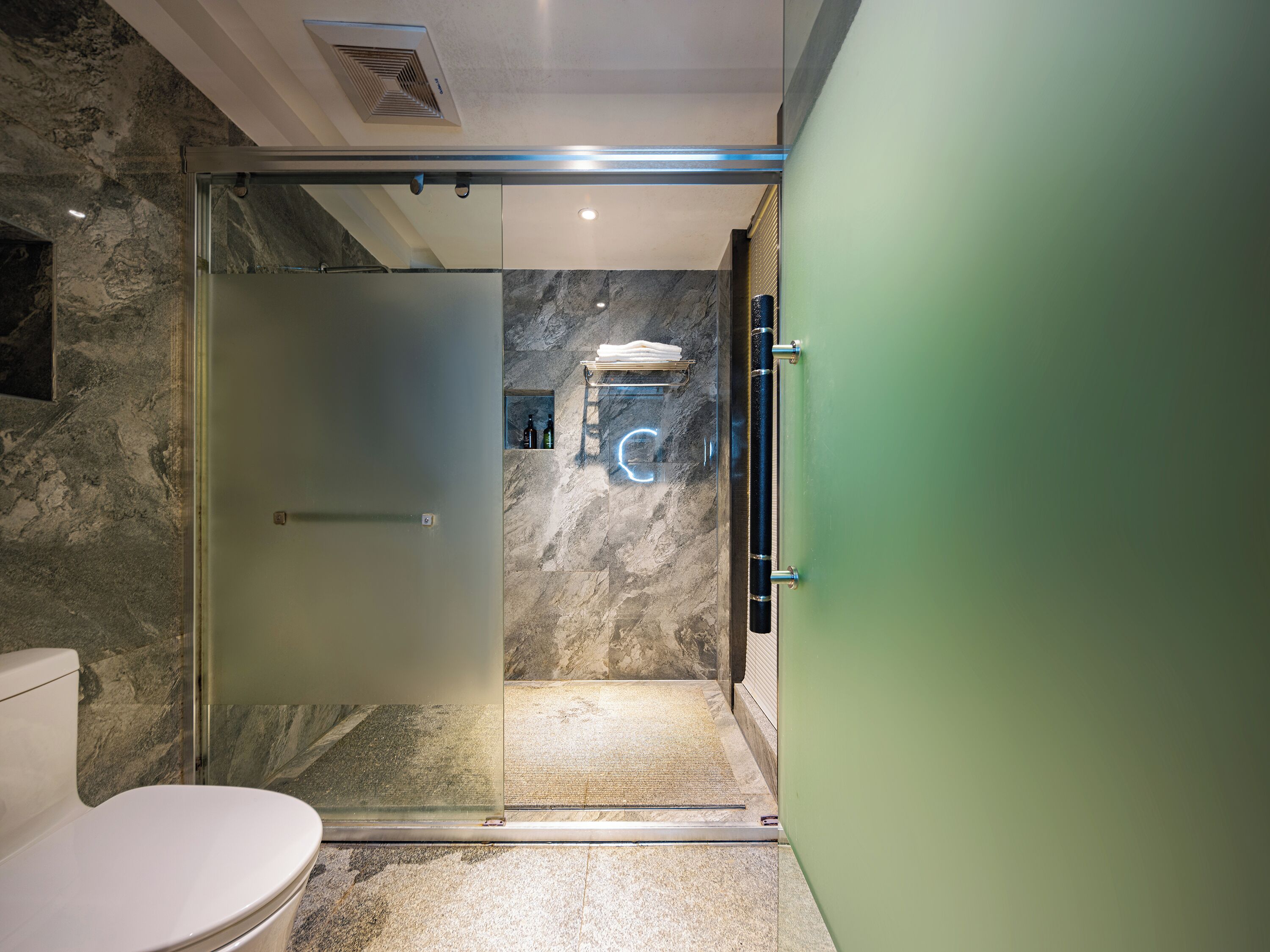 A modern bathroom with a glass shower enclosure, marble walls, and a green door.