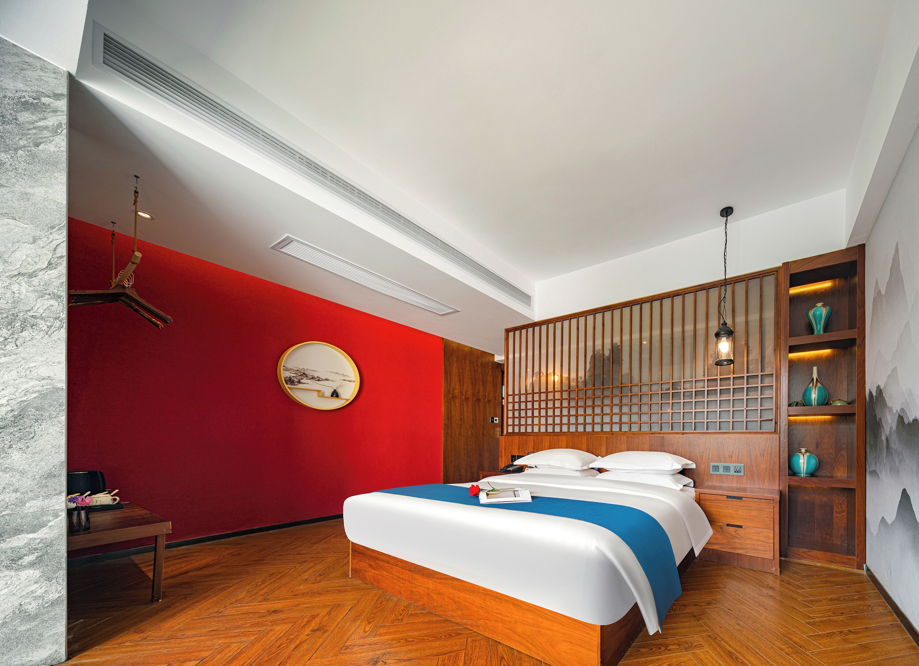 Une chambre à coucher moderne avec un lit, un mur d’accent rouge, une tête de lit en bois et une étagère décorative ornée de vases.