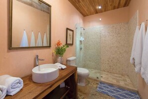 Et badeværelse med et trækommode, en hvid vask, et toilet og et bruseområde med mosaikfliser.