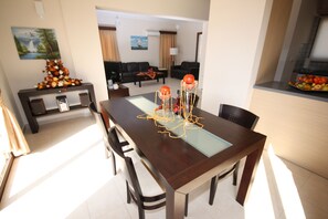 Un área de comedor con una mesa de madera oscura, cubierta de vidrio transparente y sillas modernas. Un centro de mesa decorativo con detalles naranja y rojo se encuentra sobre la mesa.