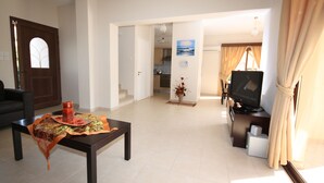 A living room with a coffee table, a sofa, a TV, and a kitchen in the background. - Seaside 2-bedroom Villa With Private Pool, Garden & Wifi Your Perfect Escape! (Pissouri)