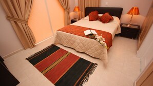 A neatly arranged bedroom with a bed, two bedside tables, a bedside lamp, a red and black striped rug, and a window with curtains. - Seaside 2-bedroom Villa With Private Pool, Garden & Wifi Your Perfect Escape! (Pissouri)