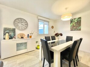 Un comedor con una mesa blanca y sillas negras, un reloj en la pared y una ventana con persianas.