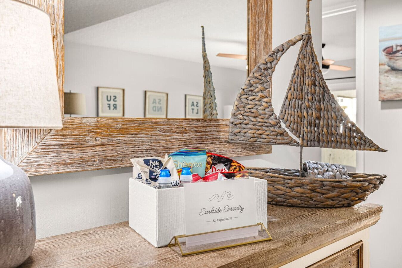 A wooden counter with a woven boat decoration, a framed nautical-themed wall, and a white box labeled "Surfside Serenity" with various items.