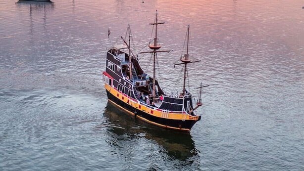 Une rivière où est amarré un navire historique, entourée de bâtiments, avec un coucher de soleil en arrière-plan.