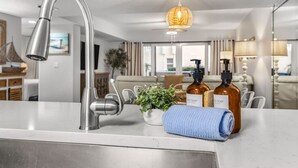 Une salle de bain moderne avec un lavabo en acier inoxydable, deux distributeurs de savon, une serviette et une plante en pot.