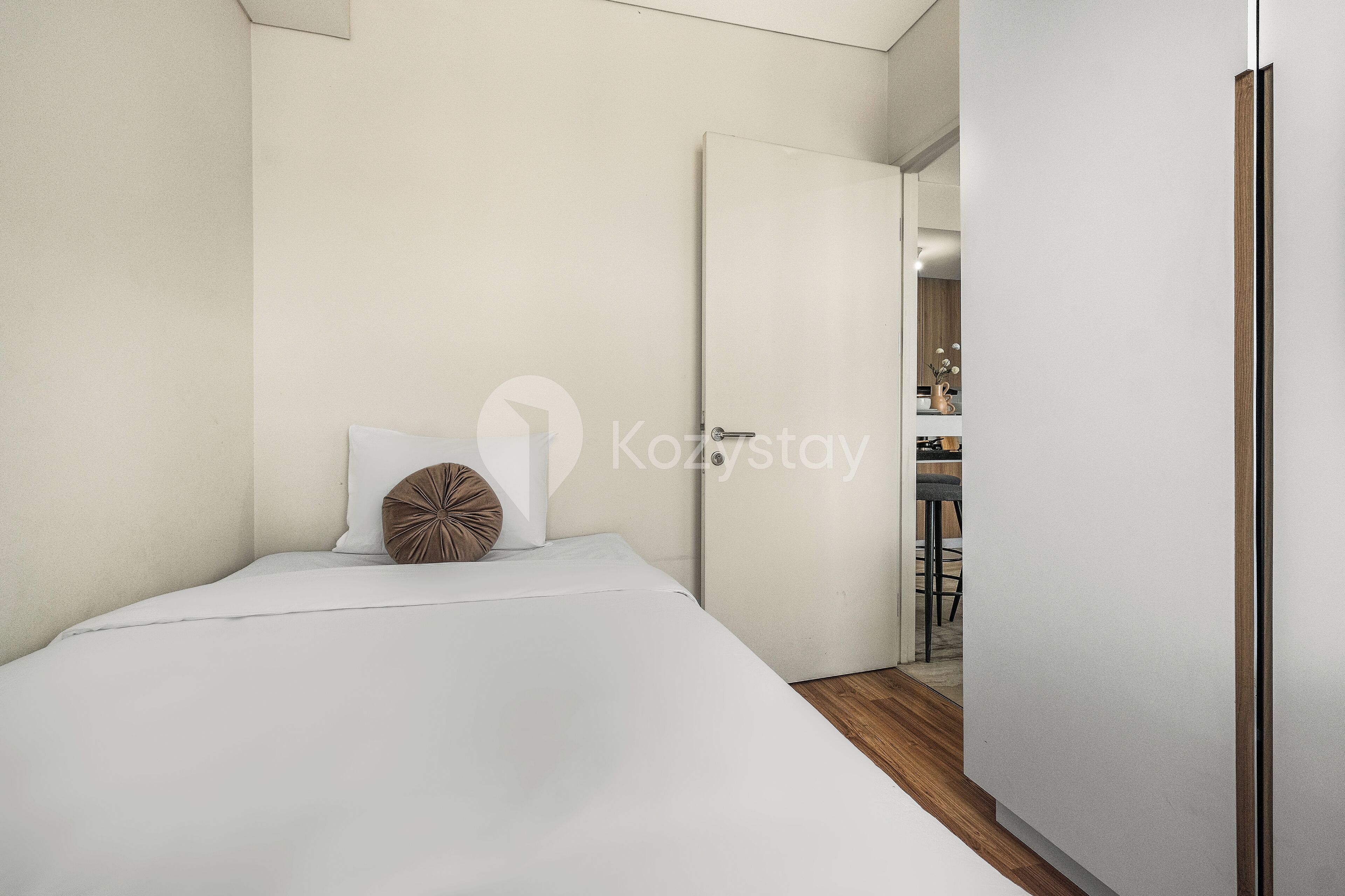 Un dormitorio moderno con una cama individual, suelo de madera y una puerta blanca que da al baño.