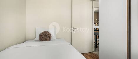 Un dormitorio moderno con una cama individual, suelo de madera y una puerta blanca que da al baño.