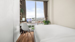 Una habitación de hotel moderna con una cama grande, un escritorio con una computadora portátil, una silla y vistas a la ciudad a través de amplios ventanales.