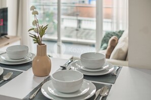A dining table set with white bowls and plates, a vase with flowers, and a view of a balcony with a railing.