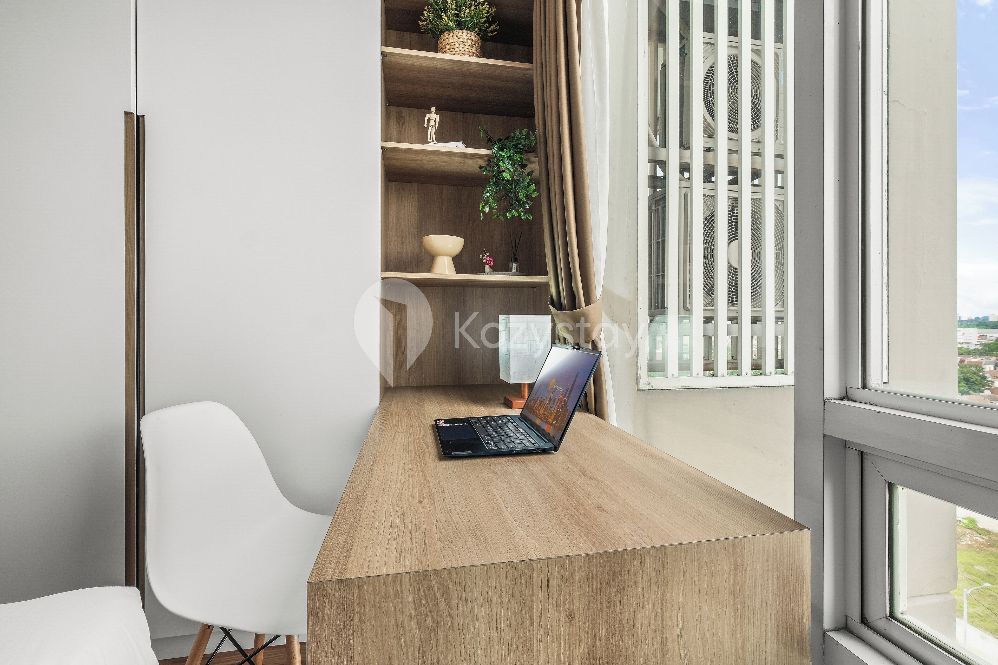 A modern office space with a laptop on a wooden desk, a white chair, and a shelving unit with decorative items.