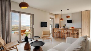 A modern living room with a sofa, two round tables, and a wicker chair. A kitchen area with a bar and a TV is visible in the background.